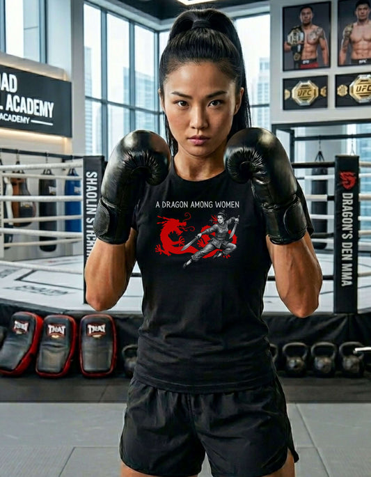 Woman in a MMA gym fists up, wearing a black t-shirt with the slogan - A Dragon among Women printed in white, above the bold graphic of a female warrior in fighting stance wielding dual swords in front of a red dragon silhouette.