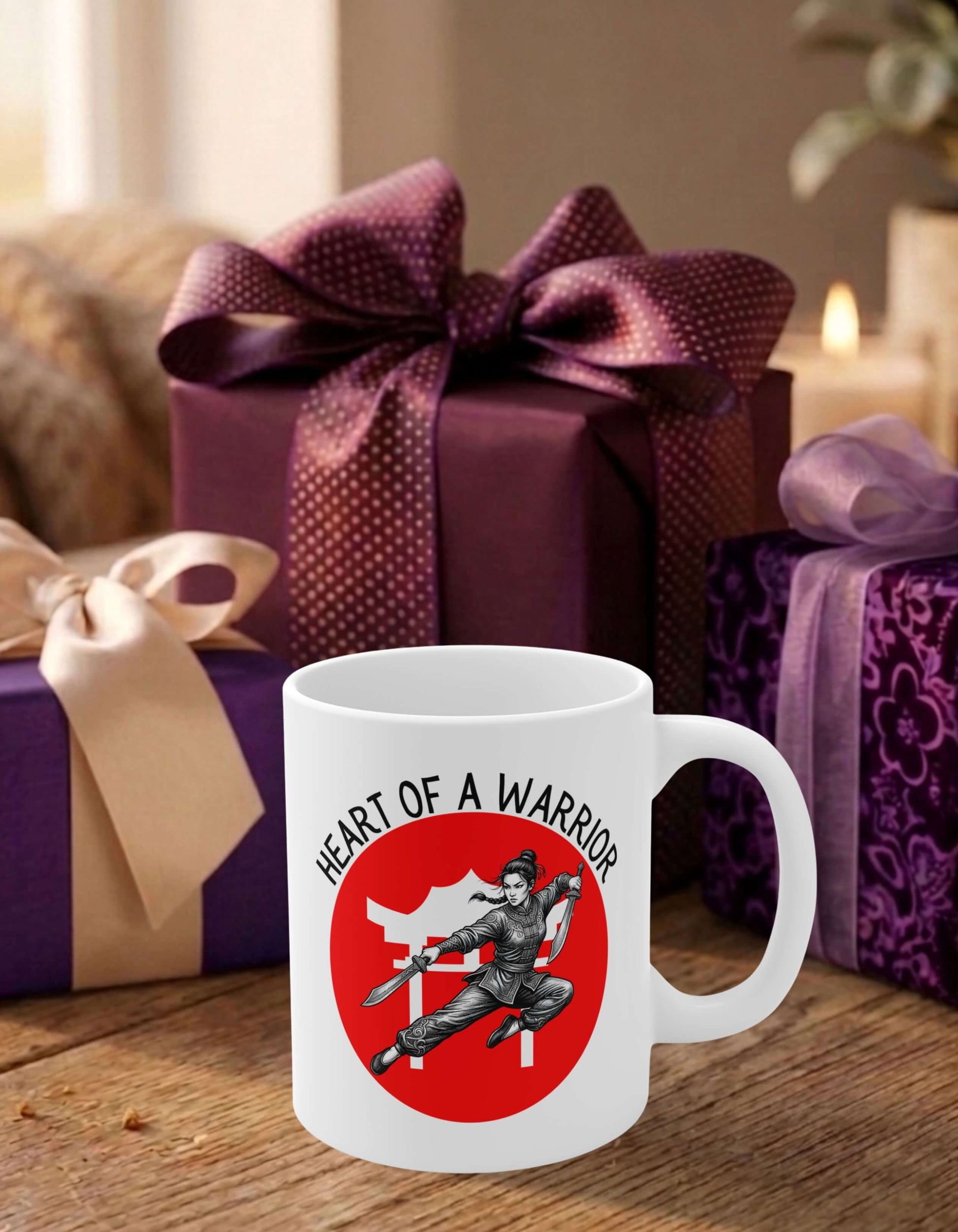 A white 11 oz ceramic mug featuring the slogan — Heart of a Warrior printed in black letters, above the graphic of a female warrior mid-air wielding twin swords in front of the silhouette of a red Chinese Temple, sits on a wooden table, surrounded by thoughtfully wrapped gifts.