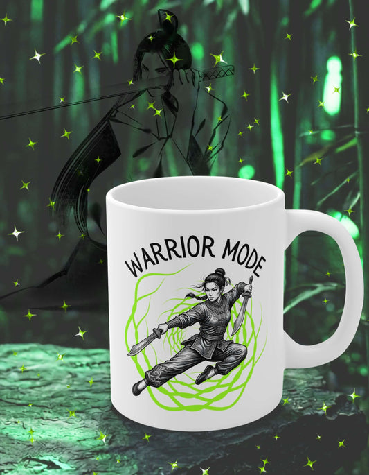 White 11 oz ceramic mug with the slogan — Warrior Mode printed in black letters, above the graphic of a female warrior mid-air wielding twin swords, surrounded by a crackling neon green energy field; sits on a stone slab with the shadow of a woman warrior in the background.