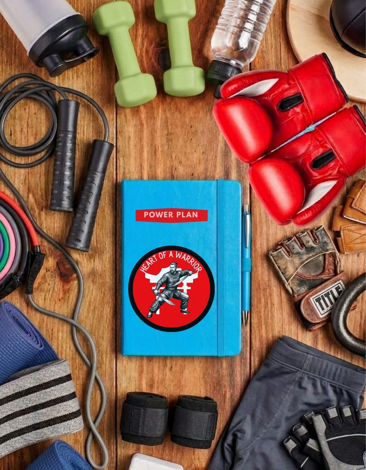 Blue Power Plan fitness journal with “Heart of a Warrior’ sticker on it, surrounded by gym equipment on a wooden surface.