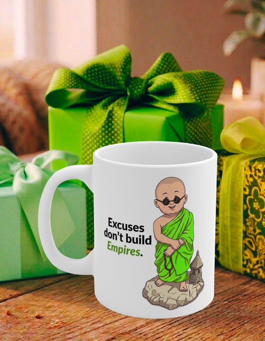 A white ceramic mug with an illustration of a monk in green robes and the text 'Excuses don't build Empires.' It is placed on a wooden table with green gift boxes in the background.