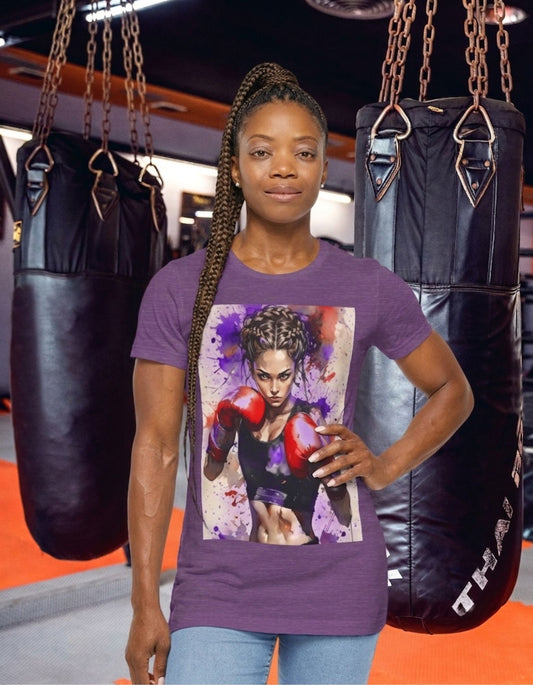 A woman stands in a gym wearing a heather team purple t-shirt with a boxer girl design, flanked by two black hanging punching bags.