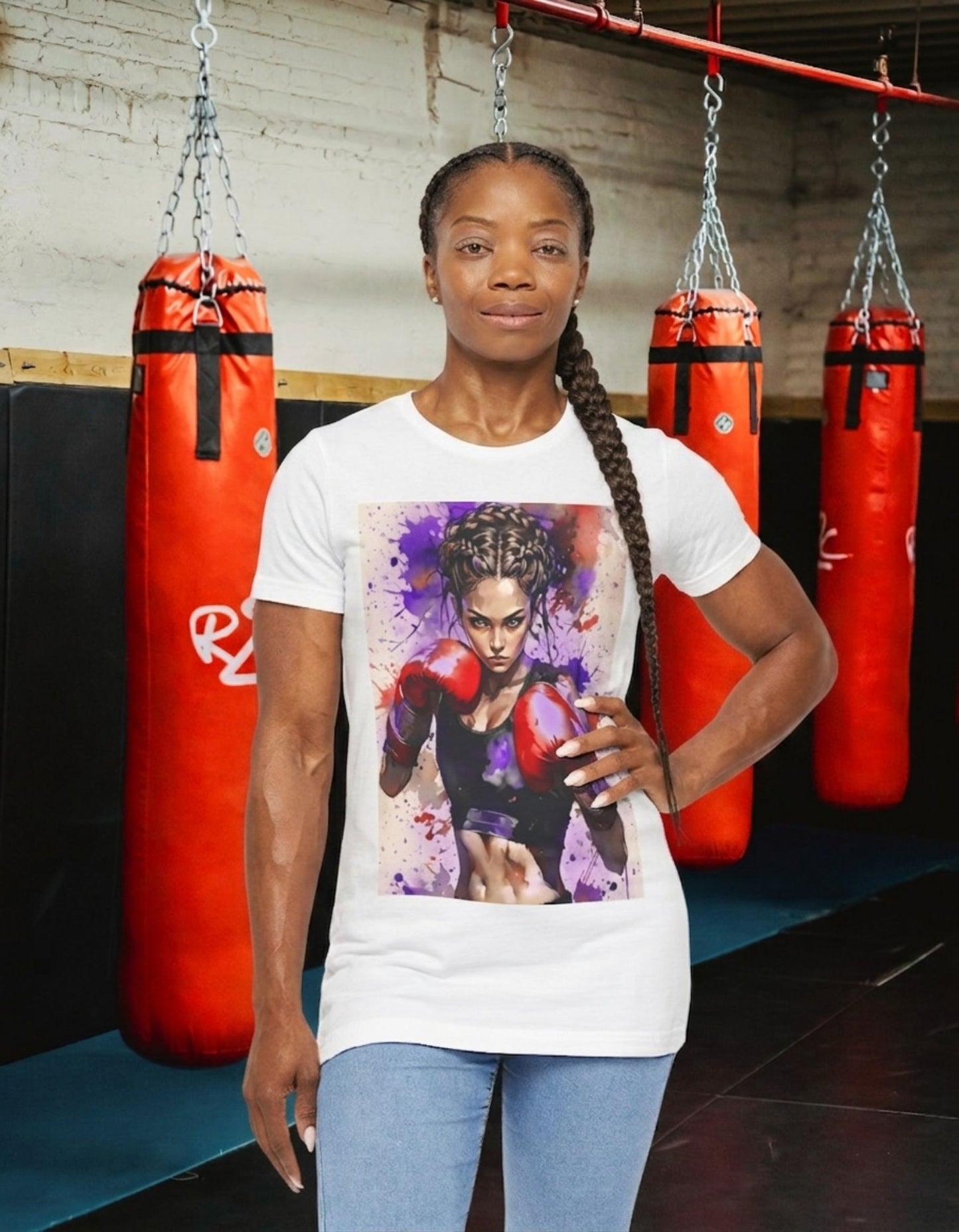A woman stands in a gym wearing a white t-shirt with a boxer girl design, behind her are hanging red punching bags.