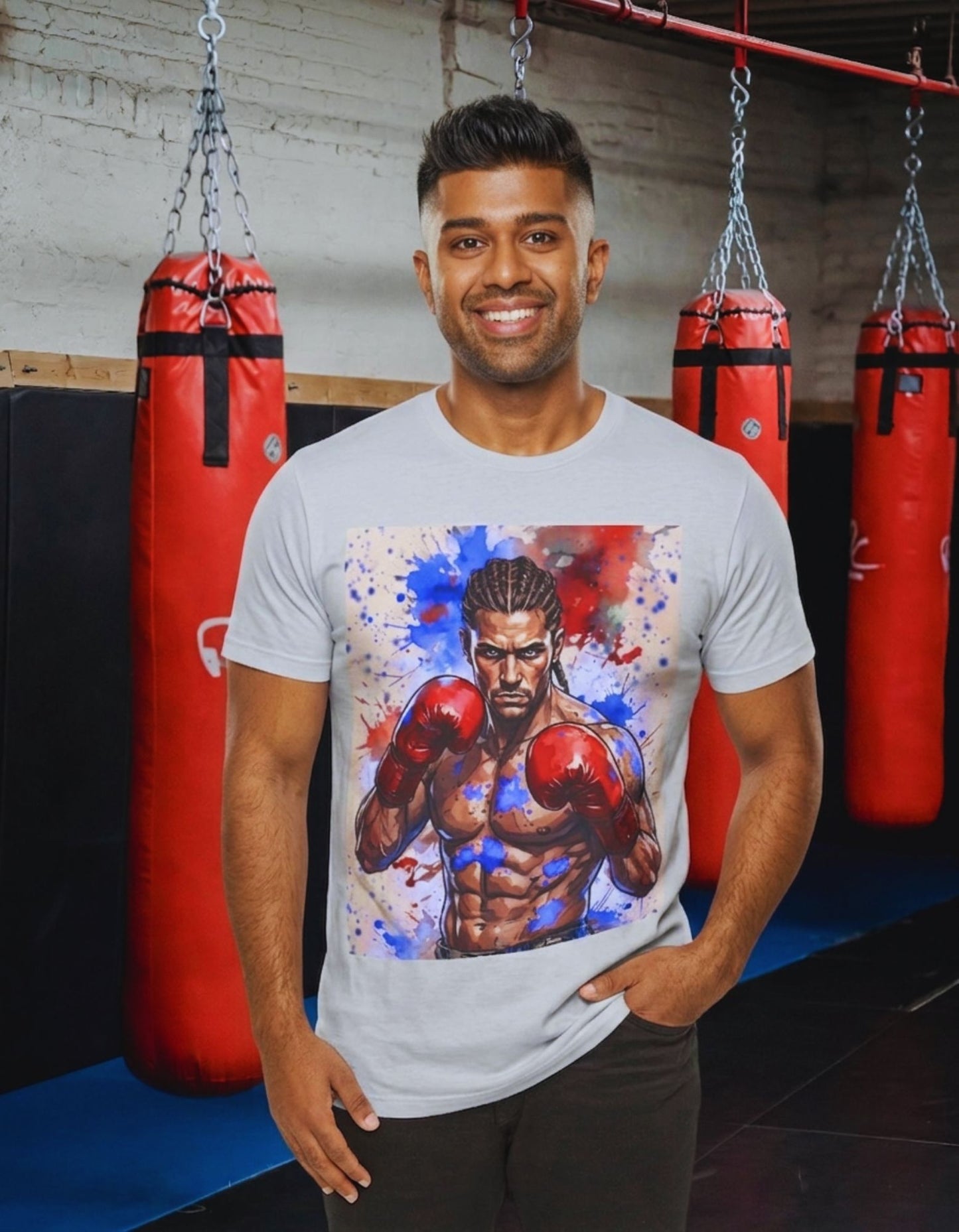 A man wearing a white t-shirt with a large graphic print of a boxer with red and blue paint splatters, standing in a gym with red hanging punching bags in the background.