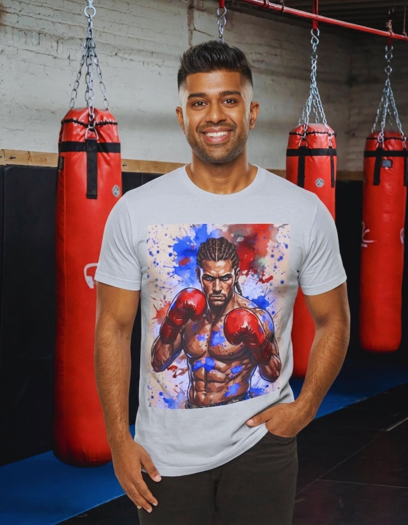 A man wearing a white t-shirt with a large graphic print of a boxer with red and blue paint splatters, standing in a gym with red hanging punching bags in the background.