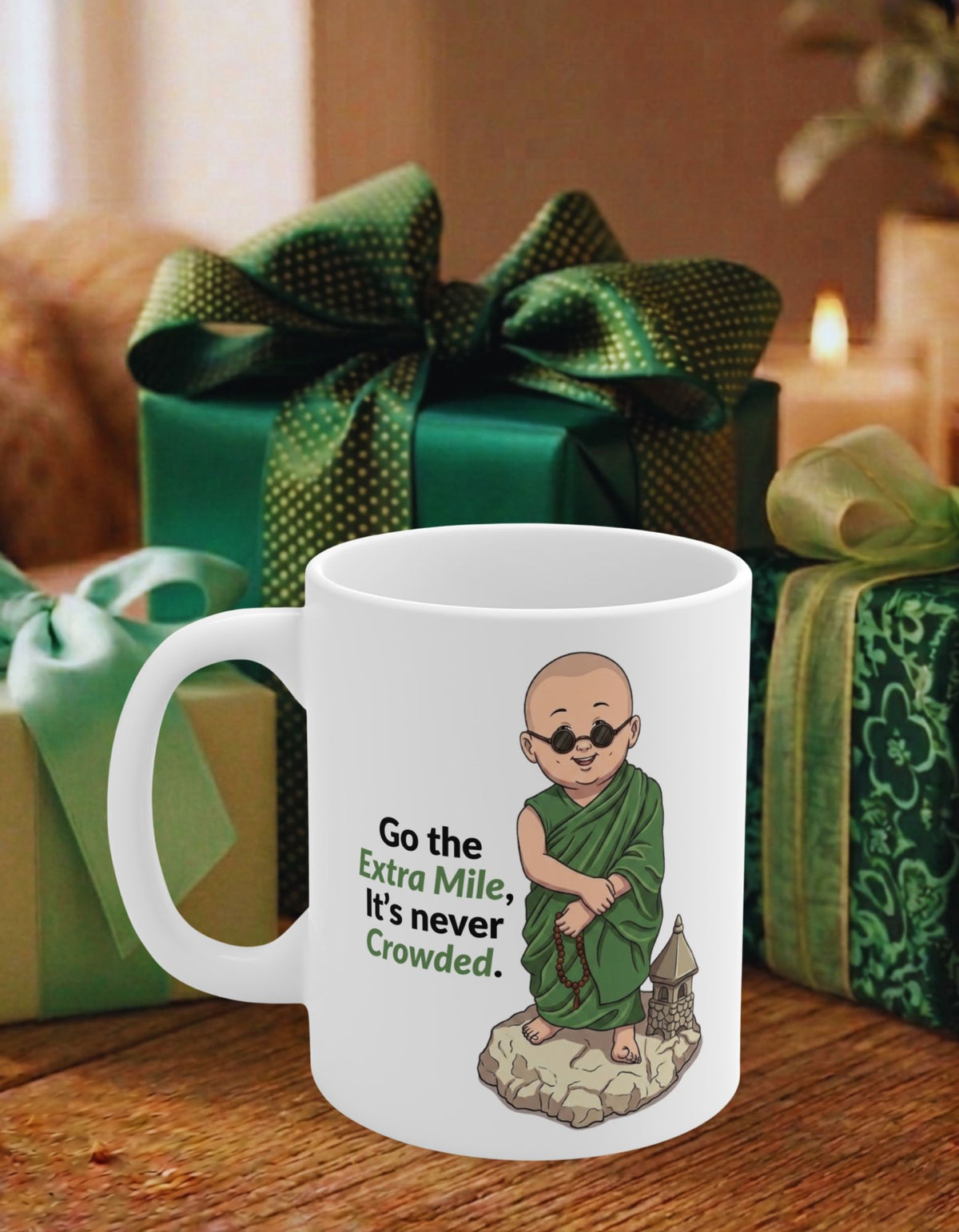 A white ceramic mug with an illustration of a monk and the text 'Go the Extra Mile, It's never Crowded.' displayed on a wooden table with green gift boxes in the background.