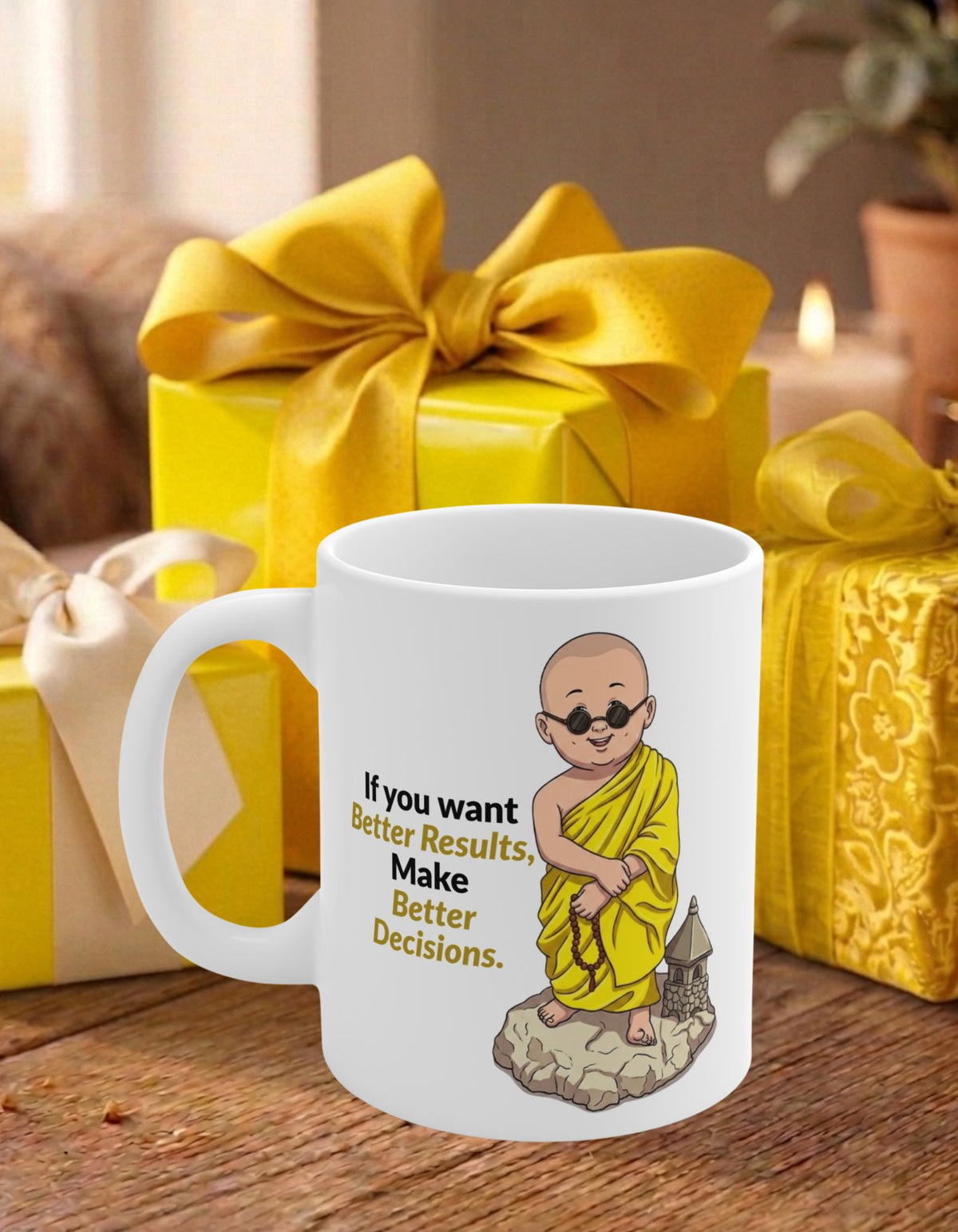 A white ceramic mug with an illustration of a monk in yellow robes and the text 'If you want Better Results, Make Better Decisions.' It is placed on a wooden table in front of yellow gift boxes with bows.