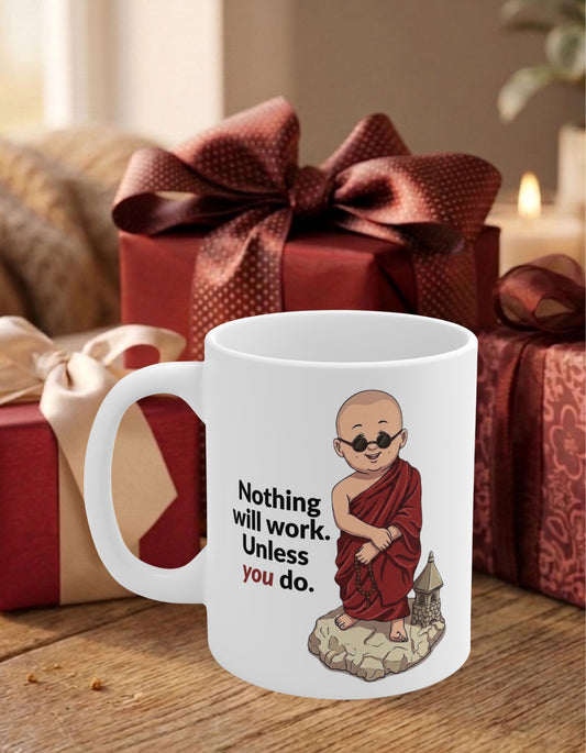 A white ceramic mug with an illustration of a monk in a red robe and the text 'Nothing will work. Unless you do.' on a table with red wrapped gifts in the background.