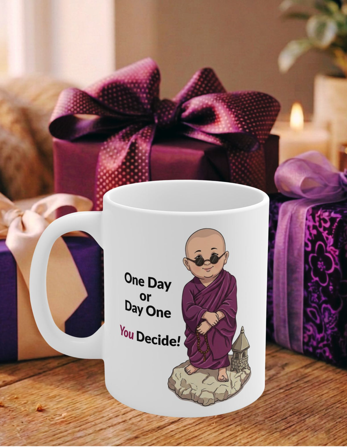 A white ceramic mug with an illustration of a monk in a purple robe and sunglasses, accompanied by the text 'One Day or Day One You Decide!'. The mug is set on a wooden table with purple gift boxes in the background.