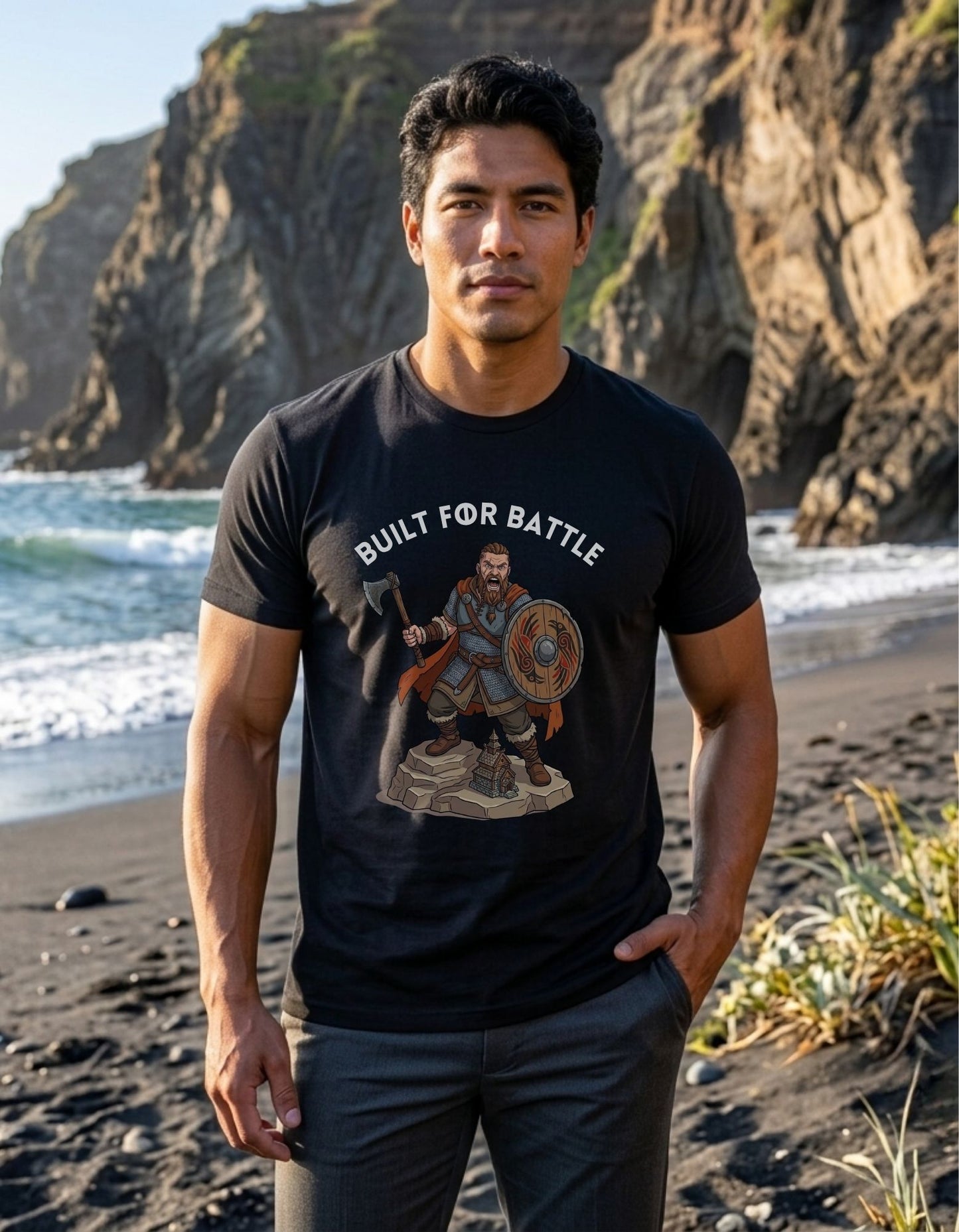 A man standing on a beach wearing a black graphic t-shirt with a Viking warrior holding an axe and shield illustration below the text 'BUILT FOR BATTLE'.