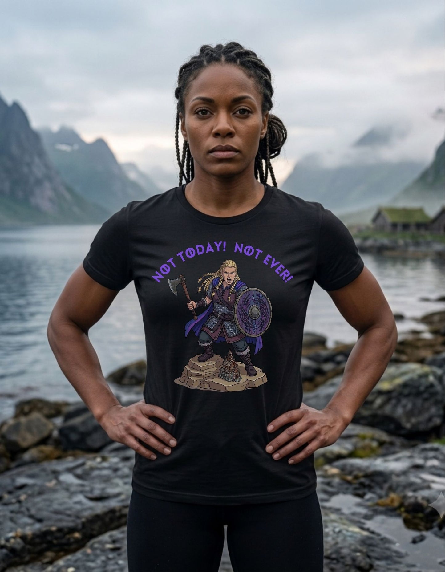 A woman stands outdoors on a rocky lakeside with misty mountains in the background, wearing a black graphic T-shirt. The shirt features a female Viking design and the text 'NOT TODAY! NOT EVER!' in purple.