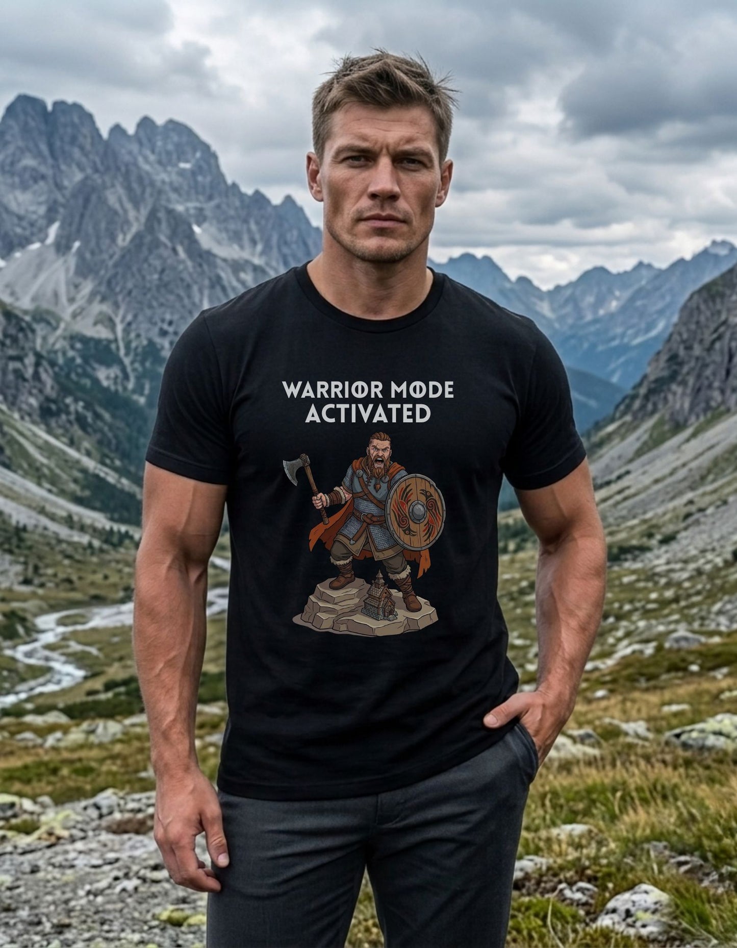 A muscular man stands in a mountain landscape wearing a black graphic t-shirt with the text 'WARRIOR MODE ACTIVATED' and a Viking warrior holding an axe and shield design below the text.